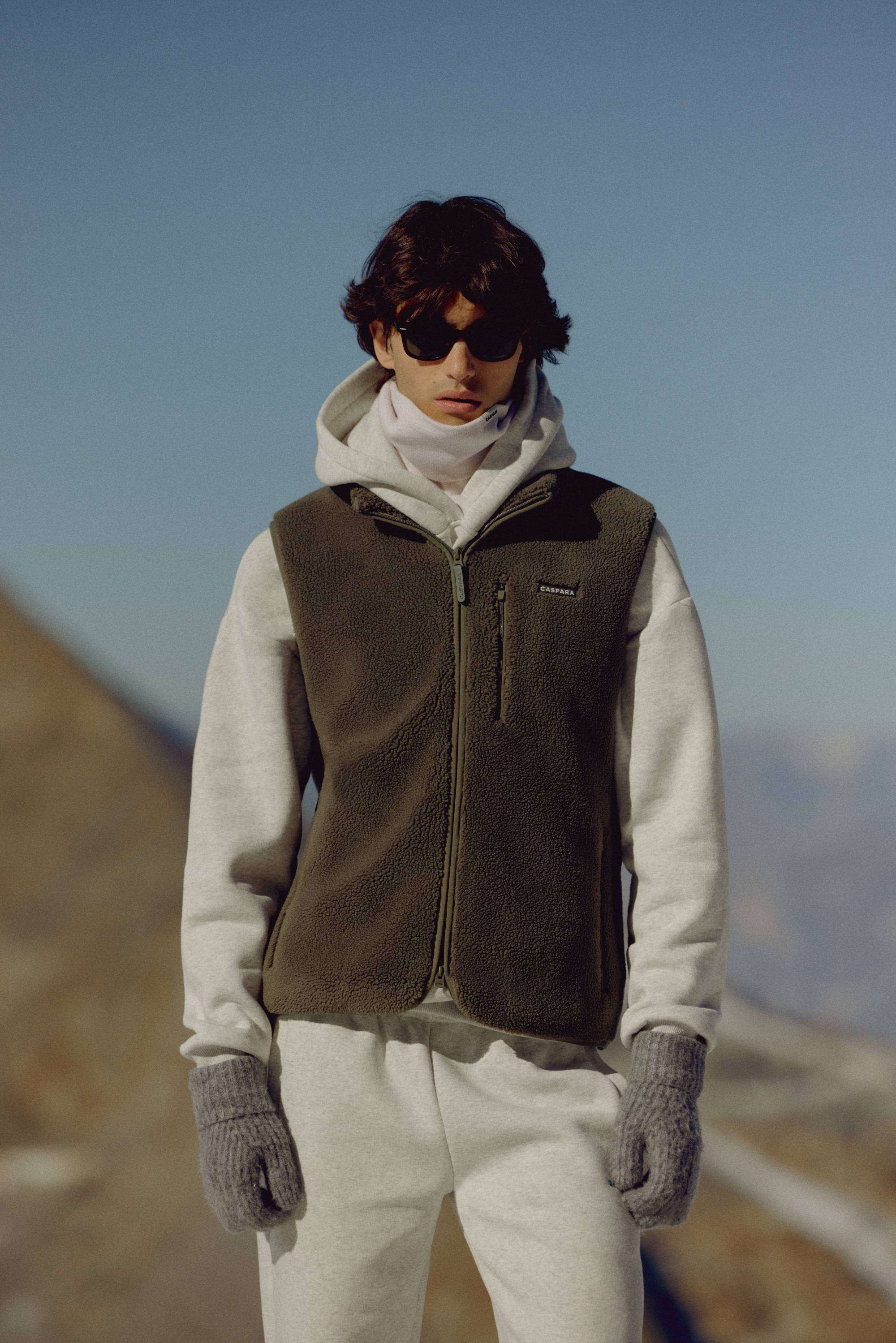 Man wearing a khaki CASPARA Cloudfleece vest in a mountain landscape.